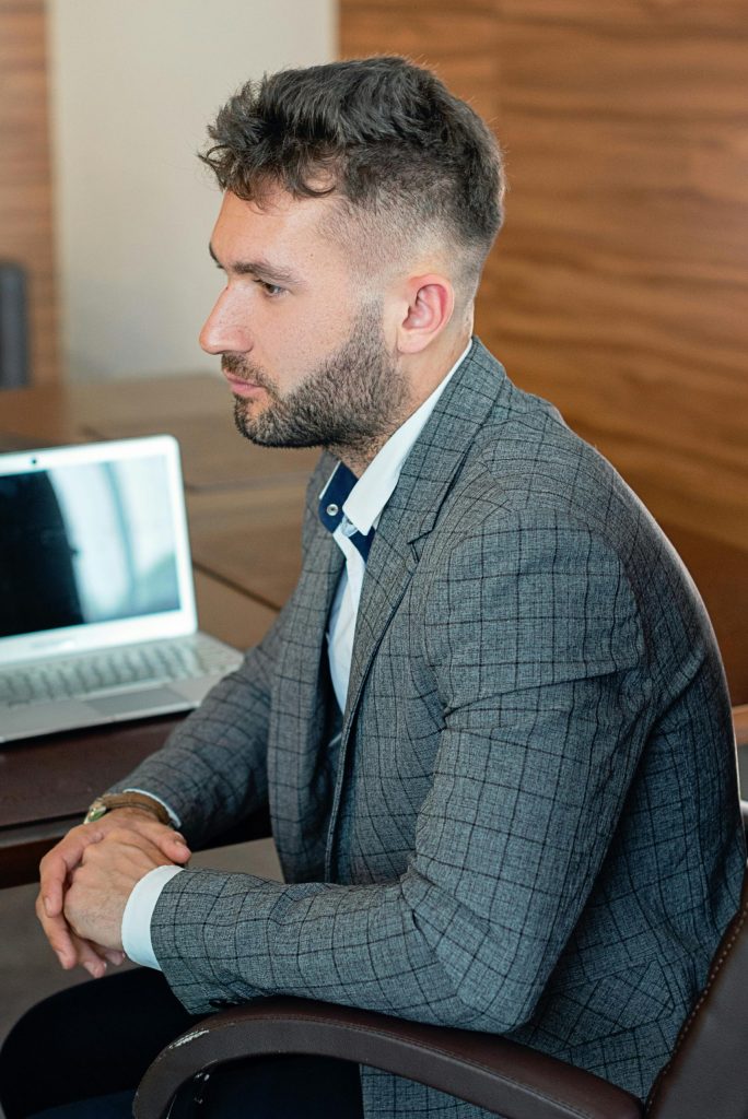Man in gray checkered suit jacket thoughtfully looking at laptop at work.