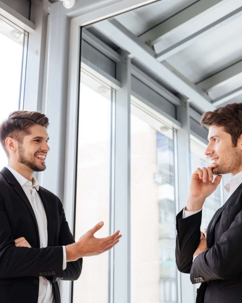 Two businessmen discussing strategy in a modern office with large windows.